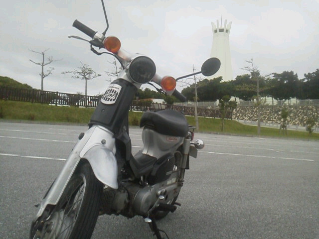 平和祈念公園の塔を背景に停車した原付バイク（ゴール地の風景）