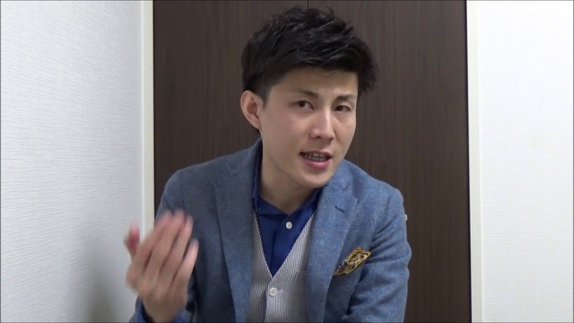ジャケット姿で手振りしながら話す本人（動画「ネットビジネスで稼ぐコツ 環境が超重要」より）