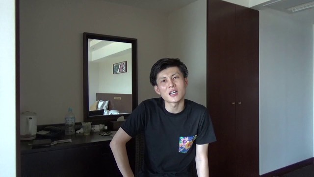 ホテルの一室で黒Tシャツ姿の本人が話す（動画「【貧困時代】お金がなくてキツい理由」より）