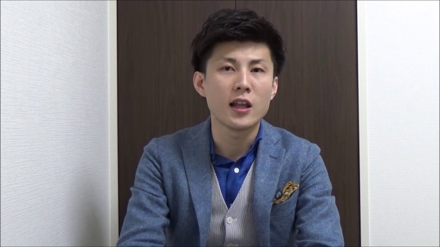 青いブレザーにポケットチーフの本人（動画「パチスロ、スロットで勝つスロプロ　ライバル対策」より）