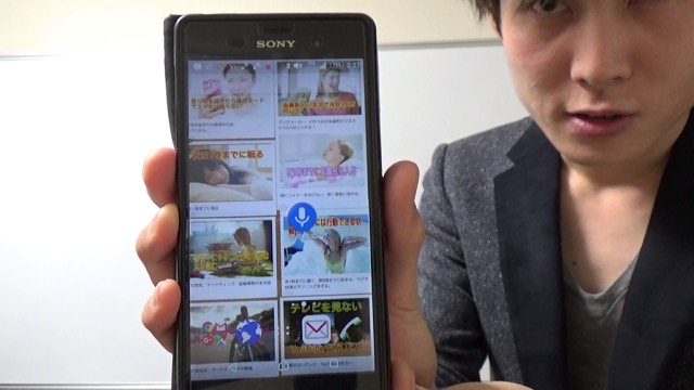 スマホの記事一覧画面を掲げて見せる本人(動画「成功できる人は行動し続ける」より)
