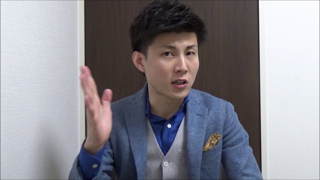青いブレザーにポケットチーフの本人（木目扉背景）（動画「パチスロ、スロットで勝つスロプロ　モデリングしよう」より）
