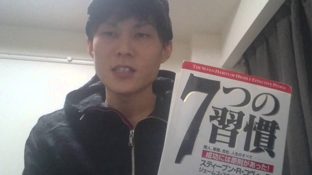 キャップを被り書籍「7つの習慣」を掲げる本人（読書の話）