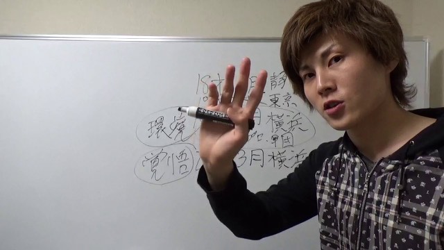 ホワイトボードの地名・日付メモを指す本人（動画「スロットで稼げるようになるまでの流れ」より）