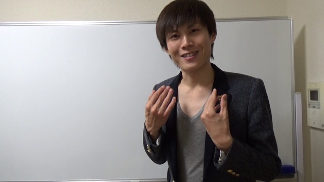 黒ジャケット姿で笑いながらホワイトボード前に立つ本人（動画「初心者向け　パチスロで稼いで生活する人　【パチスロ】」より）