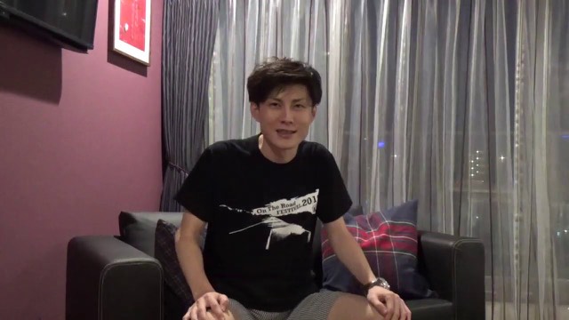 黒Tシャツ姿でソファに座る本人（夜景背景）（動画「【社畜必見】最近、僕がスロットを打ってない理由」より）