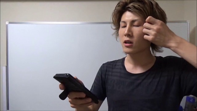 スマホを持ち目を閉じてこめかみに手を当てる本人、ホワイトボード背景（動画「Twitterで夏目五郎を検索するとアツイ…」より）