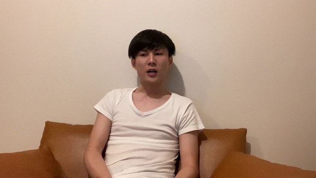 無地の壁を背景に白いTシャツでソファに座り話す本人（動画「無料で何でも提供しても自分が苦しくなるだけ」より）
