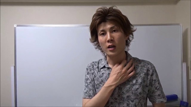 ホワイトボード前で胸に手を当てて話す柄シャツ姿の本人（動画「Facebookやってますか？【スロプロ】…」より）